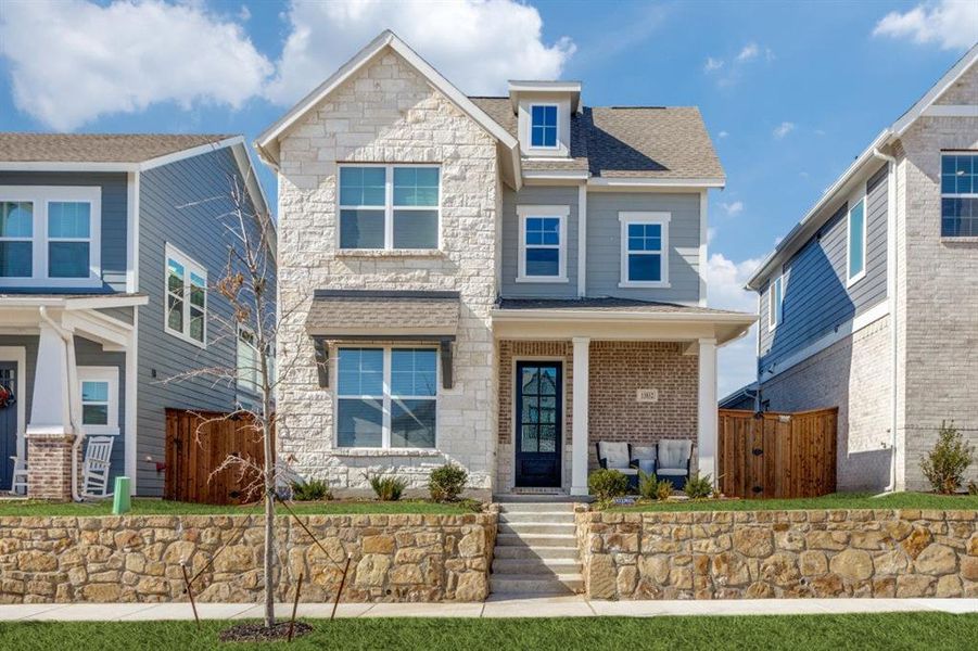 View of front of house featuring stone siding, a shingled roof, fence, and a gate