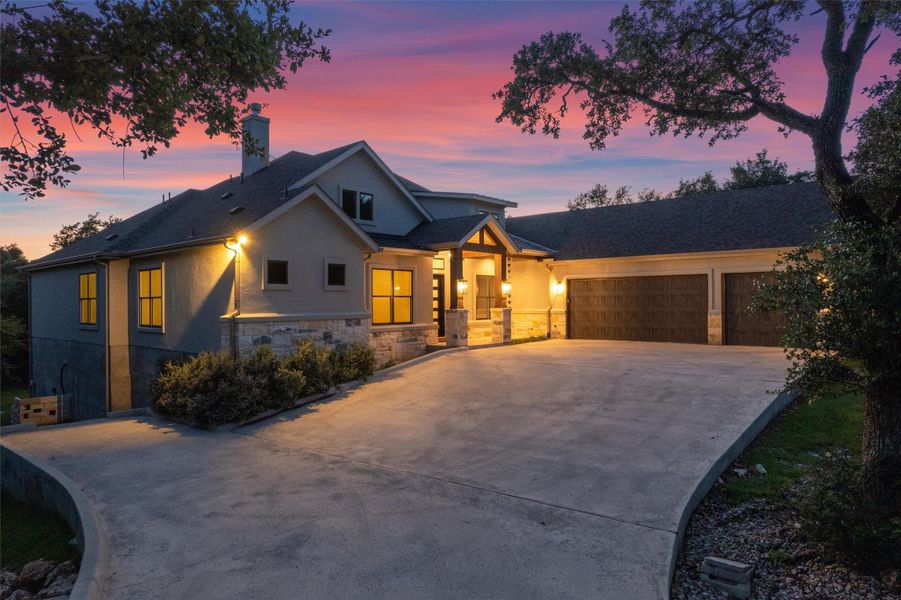 A striking modern facade with stone and stucco accents illuminates the expansive driveway and three-car garage at twilight. A striking modern facade with stone and stucco accents illuminates the expansive driveway and three-car garage at twilight.