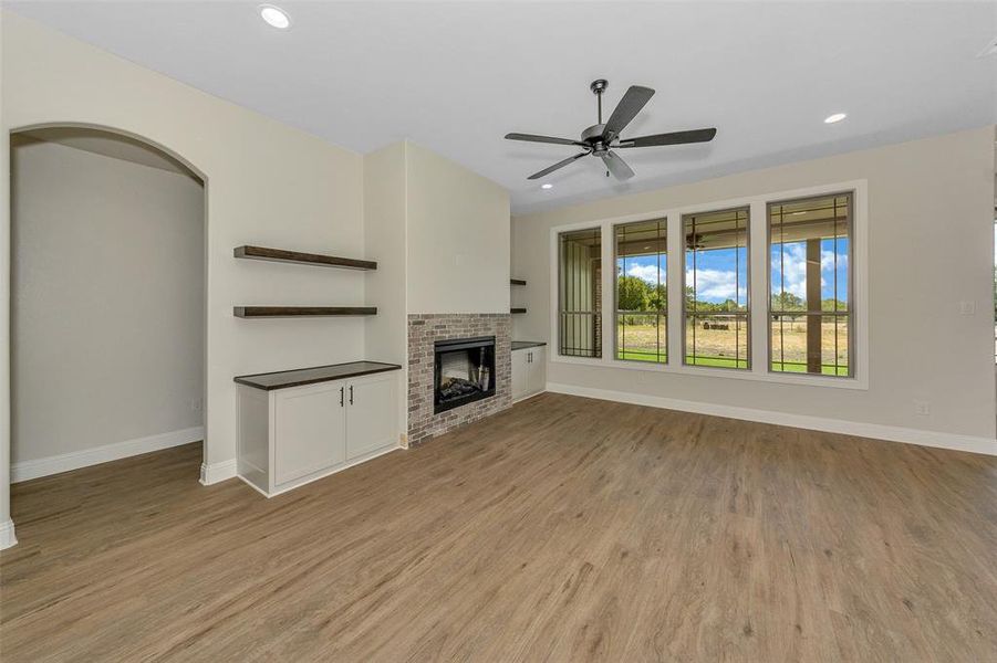 Unfurnished living room with ceiling fan, a brick fireplace, and light hardwood / wood-style floors