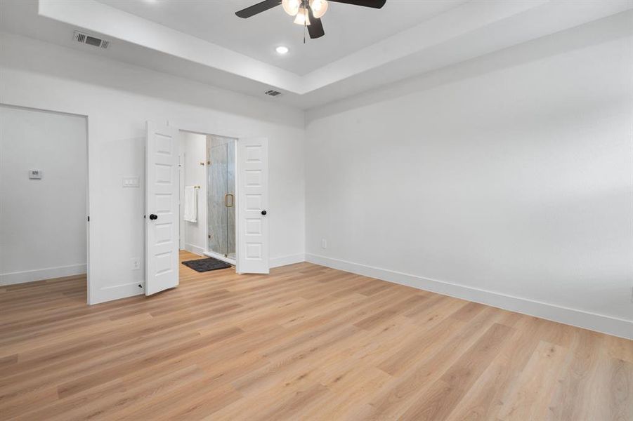 Unfurnished bedroom featuring light wood-style flooring, a raised ceiling, ceiling fan, ensuite bathroom, and recessed lighting