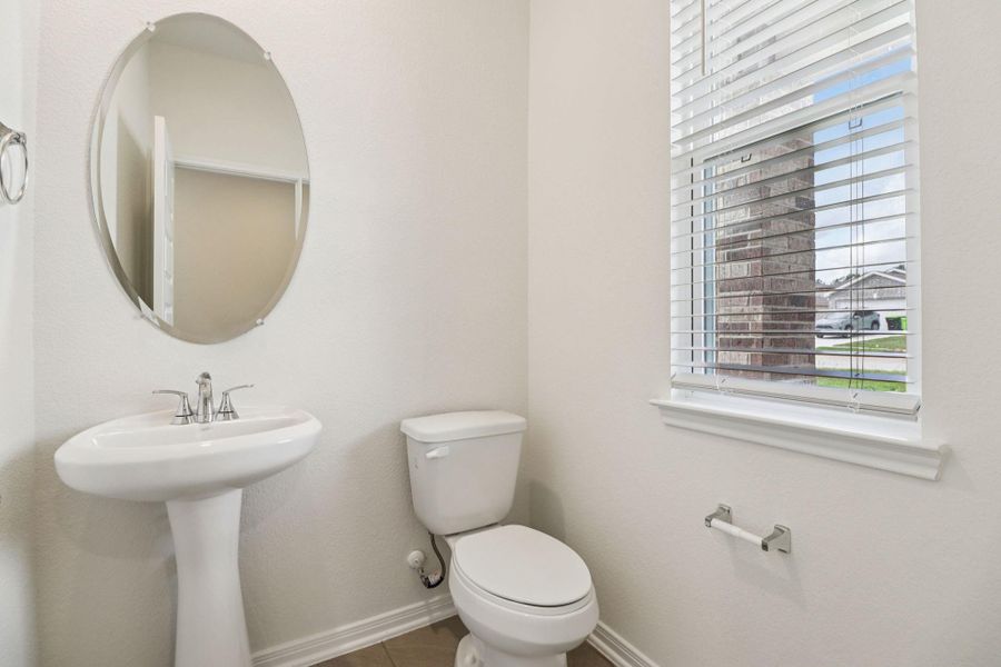 The powder room on the first floor includes a pedestal sink, mirror, toilet, and window with privacy blinds.