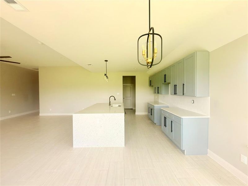 Open-concept kitchen featuring light-colored cabinetry, quartz countertops, a substantial island with an integrated sink, and wood-finish flooring