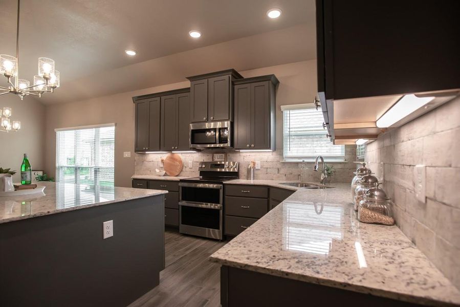 Kitchen featuring appliances with stainless steel finishes, a chandelier, light stone countertops, tasteful backsplash, and dark wood-type flooring Kitchen featuring appliances with stainless steel finishes, a chandelier, light stone countertops, tasteful backsplash, and dark wood-type flooring