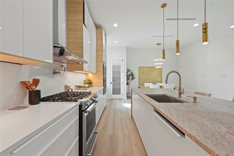 Kitchen featuring stainless steel gas stove, white cabinetry, decorative light fixtures, modern cabinets, and light wood-style flooring Kitchen featuring stainless steel gas stove, white cabinetry, decorative light fixtures, modern cabinets, and light wood-style flooring