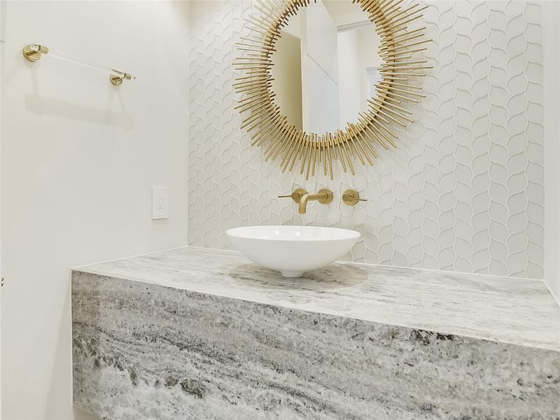 Bathroom vanity featuring a white vessel sink, a wall-mounted faucet, and a large mirror with a sunburst frame