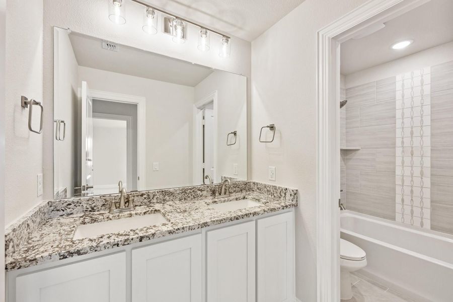 Bathroom with double sink vanity, granite countertops, white cabinets, and tiled shower-tub combo