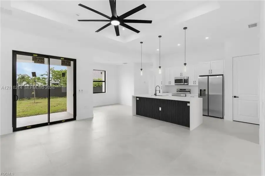 Open-concept area featuring a coffered ceiling with a black multi-blade ceiling fan, large-format tile flooring, a kitchen island with a slatted base and quartz-finish countertop, stainless steel appliances, and sliding glass doors