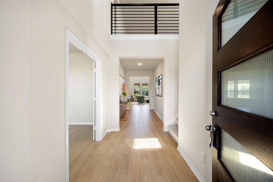 The stunning entryway features a grand, two-story ceiling that creates an immediate sense of space and light upon entry. The light wood flooring flows seamlessly through the main level while the modern black horizontal metal railing overlooks the open foyer from the second-floor balcony. *Virtually Staged The stunning entryway features a grand, two-story ceiling that creates an immediate sense of space and light upon entry. The light wood flooring flows seamlessly through the main level while the modern black horizontal metal railing overlooks the open foyer from the second-floor balcony. *Virtually Staged