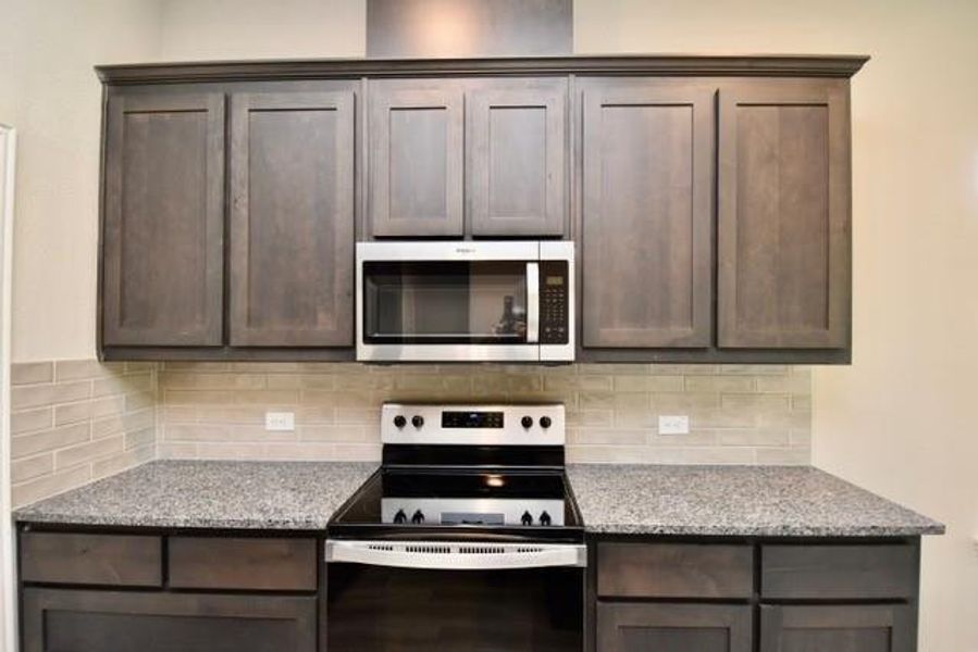 Kitchen with stainless steel appliances, dark brown cabinetry, and decorative backsplash Kitchen with stainless steel appliances, dark brown cabinetry, and decorative backsplash