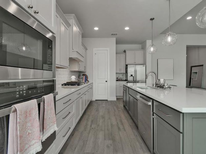 Kitchen with stainless steel appliances, gray cabinetry, decorative light fixtures, light wood-type flooring, and decorative backsplash Kitchen with stainless steel appliances, gray cabinetry, decorative light fixtures, light wood-type flooring, and decorative backsplash