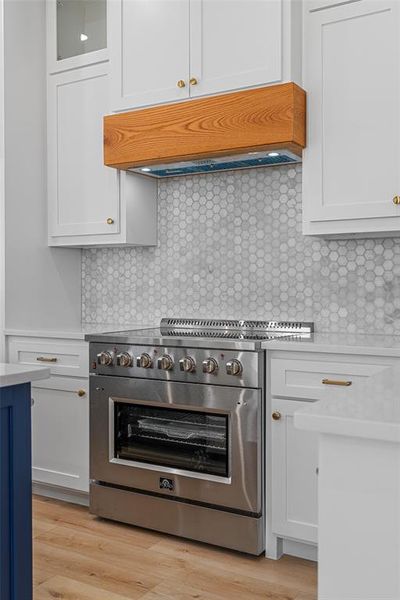 Kitchen featuring decorative backsplash, white cabinets, light hardwood / wood-style floors, and high end stove