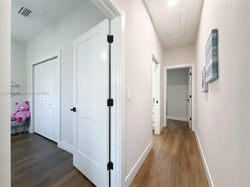 Interior hallway featuring wood-finish flooring, two-panel shaker style doors, and matte black hardware