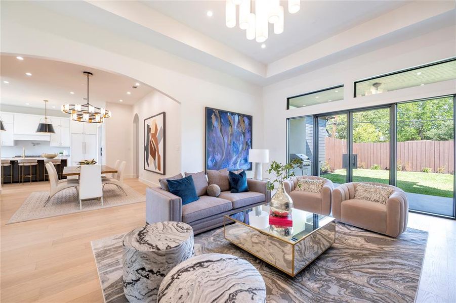 Living room featuring sink, light hardwood / wood-style floors, a towering ceiling, and an inviting chandelier