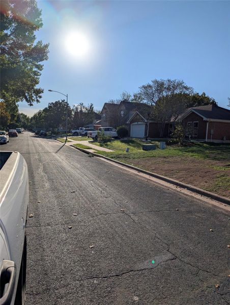 View of asphalt street featuring curbs, street lights, a residential view, and sidewalks