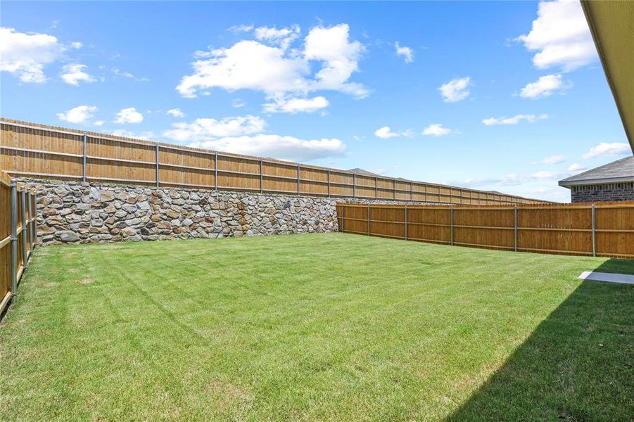 Expansive backyard featuring a manicured lawn, full privacy fencing, and a stone retaining wall