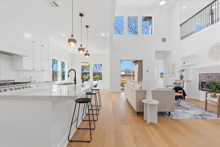 A chef-inspired kitchen to the left showcasing a 48 in stove, porcelain countertops and stylish pendant lighting. While the cozy living room to the right features an electric fireplace, soaring 21-foot ceilings, and picture windows that illuminate with natural light.