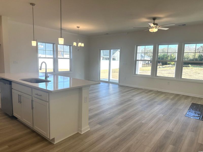 Kitchen featuring pendant lighting, open floor plan, light wood-type flooring, white cabinetry, and crown molding