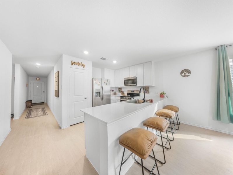 Kitchen with light countertops, a kitchen bar, light wood-style floors, stainless steel appliances, and a peninsula
