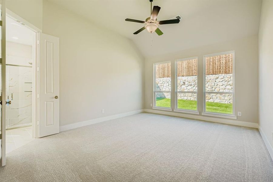 Empty room featuring light carpet, vaulted ceiling, and a ceiling fan