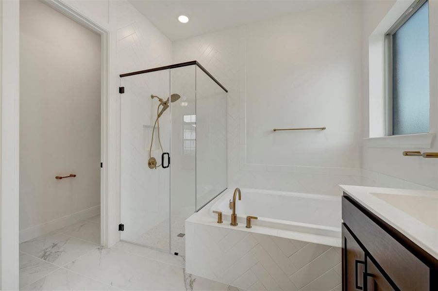 Bathroom featuring a frameless glass shower enclosure with matte black trim, a built-in bathtub with herringbone tile surround, a single vanity with dark cabinetry, gold-finish fixtures, and large-format tile flooring