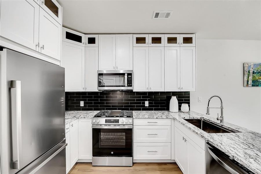 Kitchen with light granite counters, white cabinets, appliances with stainless steel finishes, and sink