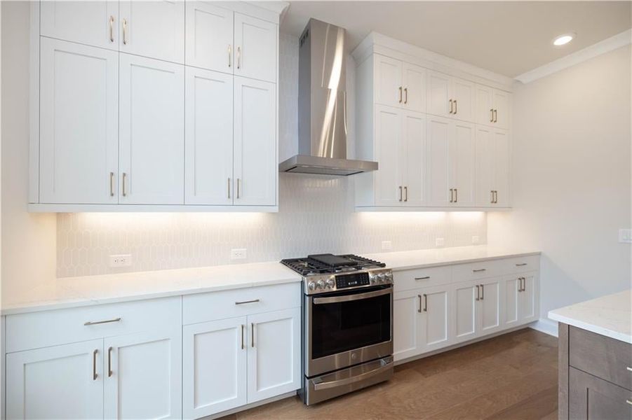 Kitchen featuring white cabinetry, stainless steel range with gas cooktop, decorative backsplash, and wall chimney exhaust hood