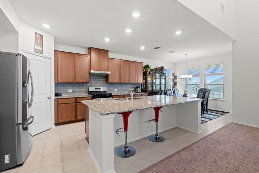 Open-concept kitchen featuring wood cabinetry, granite countertops, stainless steel appliances, and a tile backsplash