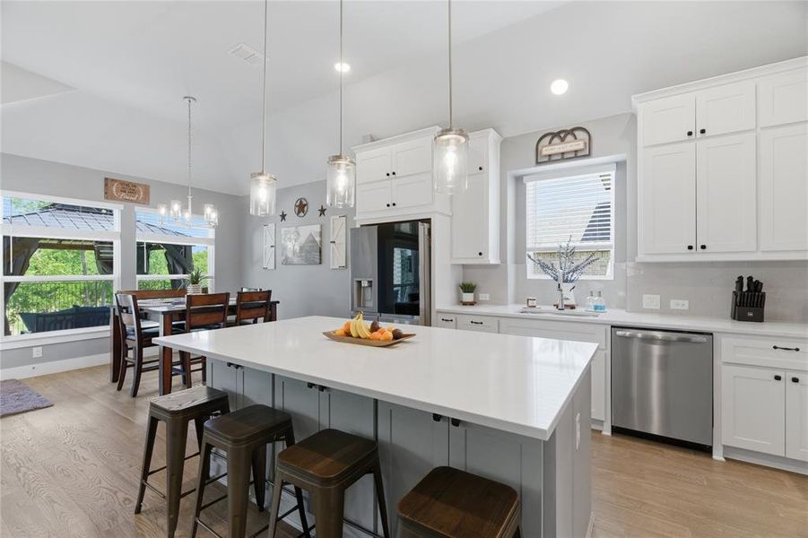 Kitchen featuring a large central island with seating, white shaker-style cabinetry, and stainless steel appliances