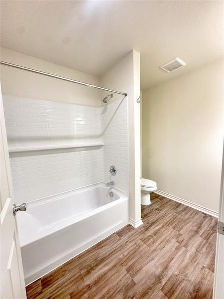 Bathroom with hardwood / wood-style flooring, tiled shower / bath combo, and toilet