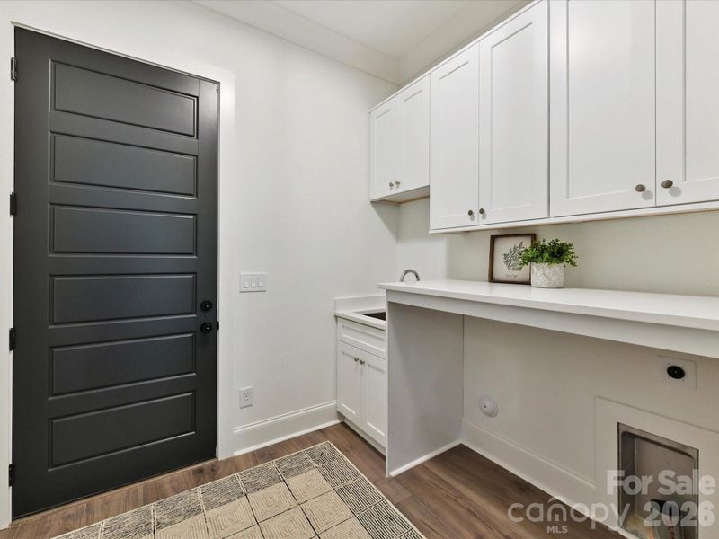 Functional laundry room with built-in cabinetry, utility sink, folding counter, and convenient exterior door access.