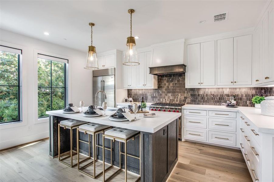 Kitchen featuring a kitchen island with sink, white cabinetry, a kitchen bar, premium appliances, and light hardwood / wood flooring