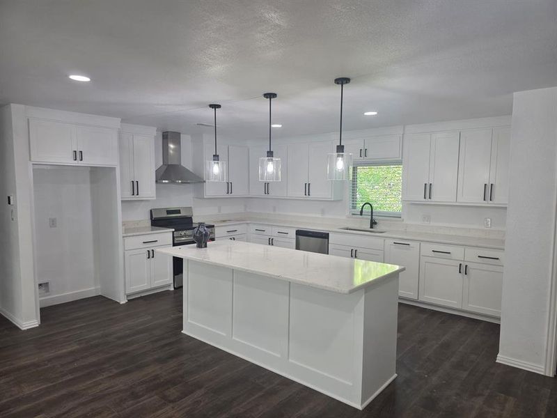 Kitchen with appliances with stainless steel finishes, wall chimney exhaust hood, a kitchen island, white cabinetry, and dark wood-type flooring Kitchen with appliances with stainless steel finishes, wall chimney exhaust hood, a kitchen island, white cabinetry, and dark wood-type flooring