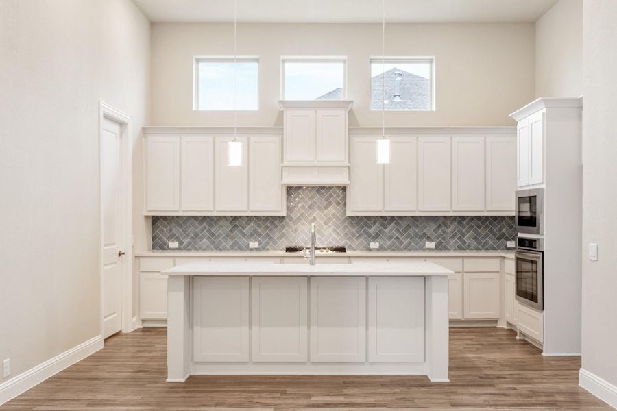 Kitchen with white cabinets, center island, gray herringbone tile backsplash, and hardwood floors