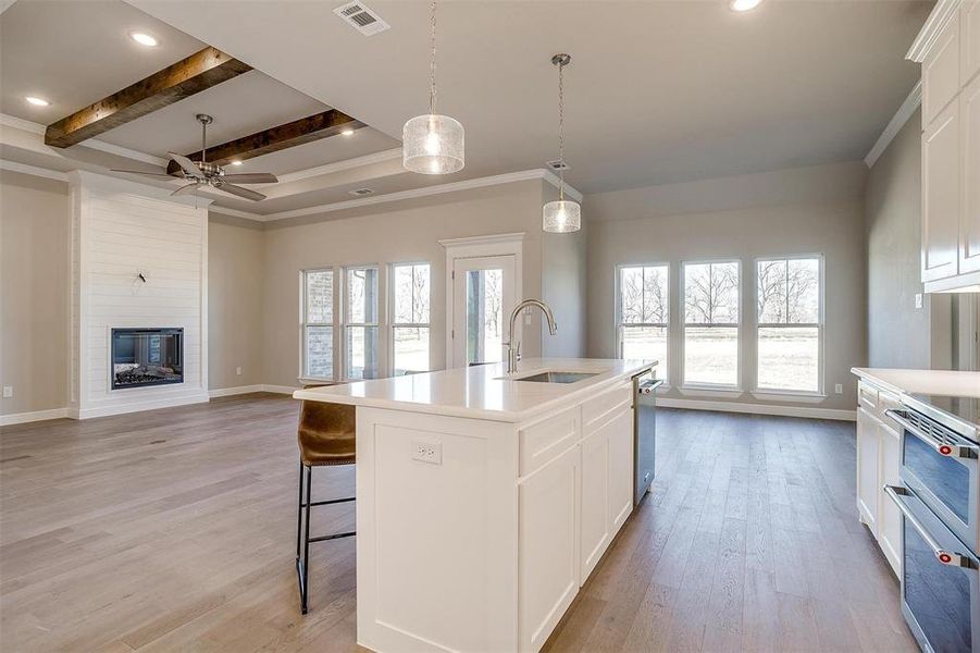 Kitchen with a fireplace, beamed ceiling, white cabinetry, an island with sink, and sink