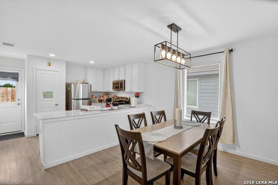 A well-lit dining area features a modern chandelier and ample space, flowing into a functional kitchen. A well-lit dining area features a modern chandelier and ample space, flowing into a functional kitchen.