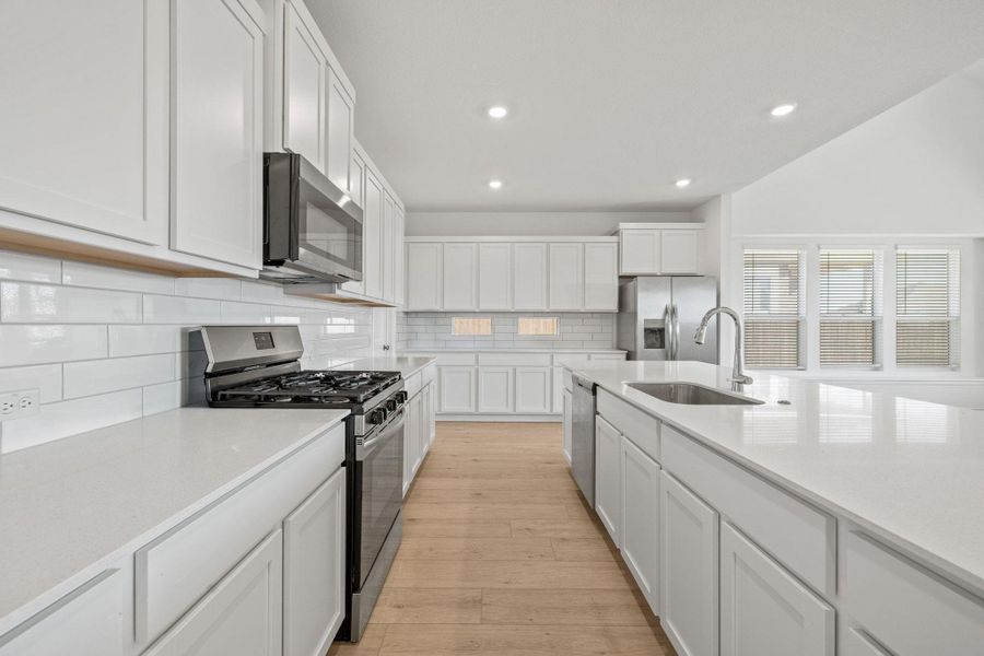 Kitchen featuring stainless steel appliances, white cabinetry, backsplash, light stone countertops, and recessed lighting