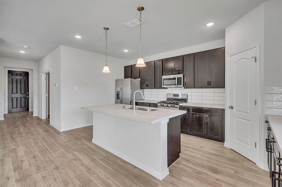 Kitchen with stainless steel appliances, pendant lighting, decorative backsplash, sink, and light hardwood / wood-style flooring