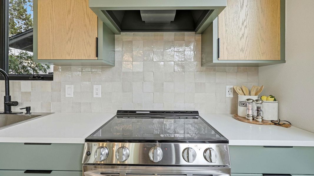 Kitchen with stainless steel electric range oven, backsplash, light wood finish cabinets, and light stone counters