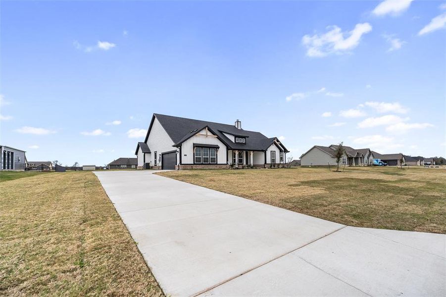 View of front facade featuring concrete driveway, a front lawn, a garage, and stone siding