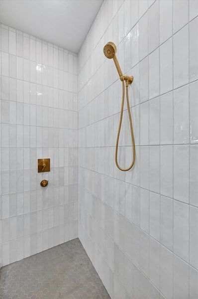 Walk-in shower featuring white subway tile walls, a hand-held shower fixture, and a wall-mounted shower control with a brushed gold finish