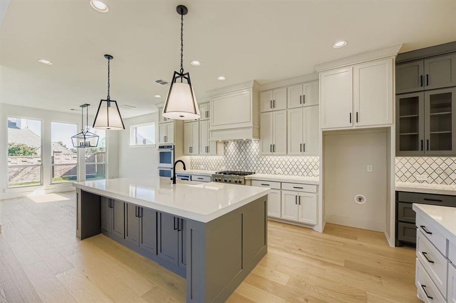 Kitchen featuring white cabinets, glass insert cabinets, light wood-style floors, decorative light fixtures, and light stone countertops Kitchen featuring white cabinets, glass insert cabinets, light wood-style floors, decorative light fixtures, and light stone countertops