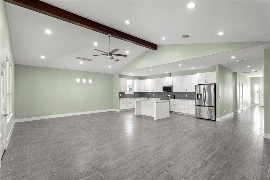 Kitchen with open floor plan, backsplash, white cabinetry, stainless steel appliances, and ceiling fan