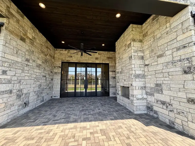 A covered stone patio features brick pavers and a built-in outdoor fireplace.