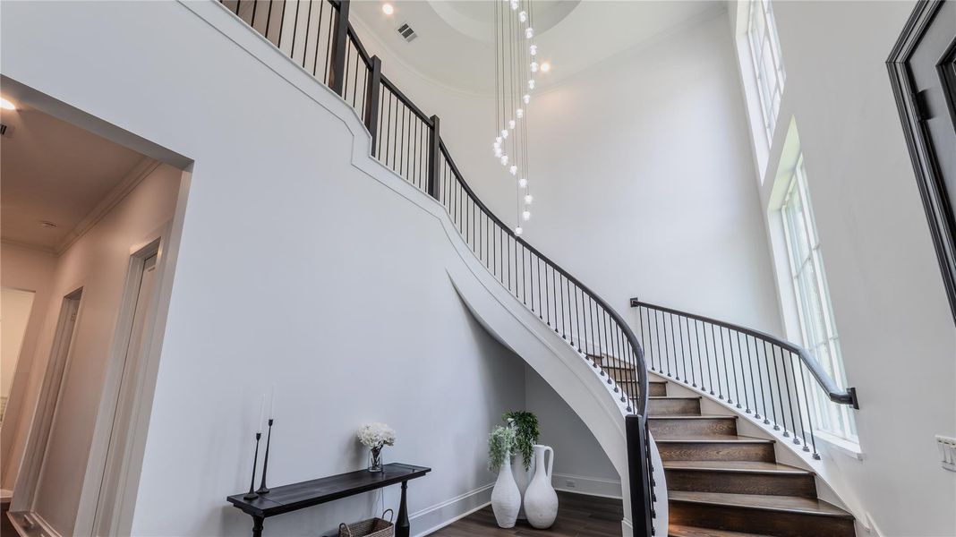 This photo showcases an elegant foyer with a grand, curved staircase featuring dark wood steps and sleek railing. The space is accentuated by high ceilings, large windows, and a contemporary chandelier, creating an inviting and luxurious entryway.