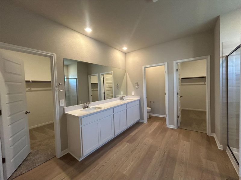 Bathroom with a walk in closet, double vanity, a shower stall, wood finished floors, and recessed lighting Bathroom with a walk in closet, double vanity, a shower stall, wood finished floors, and recessed lighting