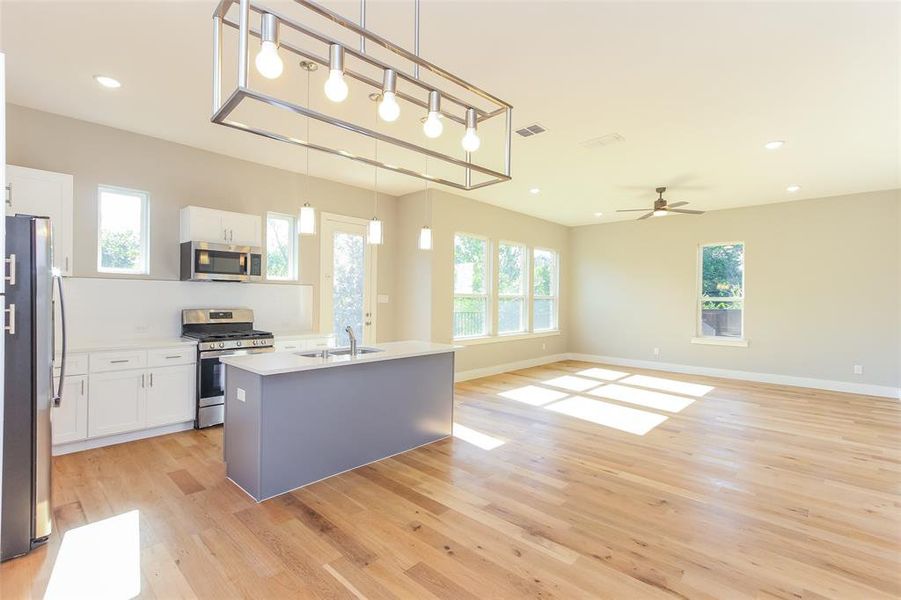 Kitchen featuring sink, hanging light fixtures, stainless steel appliances, white cabinets, and a center island with sink