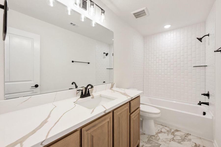 Bathroom with marble countertop, wood vanity, white tile tub surround, and black fixtures on marble-look floors