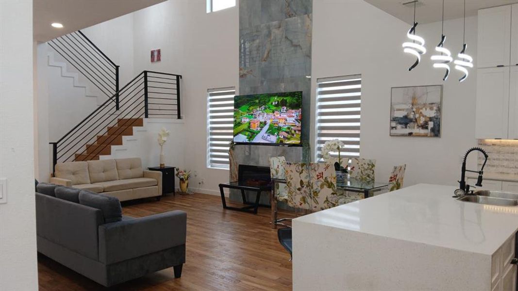 Open-concept living space featuring wood-finish flooring, a two-story ceiling, and an open staircase with black metal railings