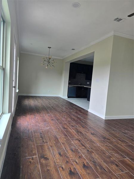 Empty room featuring a chandelier, wood-type flooring, crown molding, and baseboards