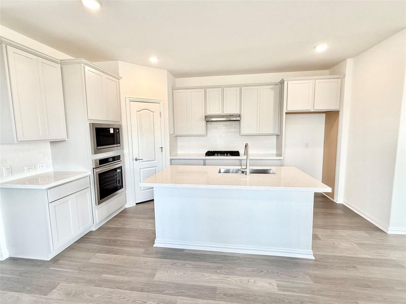 Kitchen with backsplash, light stone counters, light wood-style floors, appliances with stainless steel finishes, and recessed lighting Kitchen with backsplash, light stone counters, light wood-style floors, appliances with stainless steel finishes, and recessed lighting